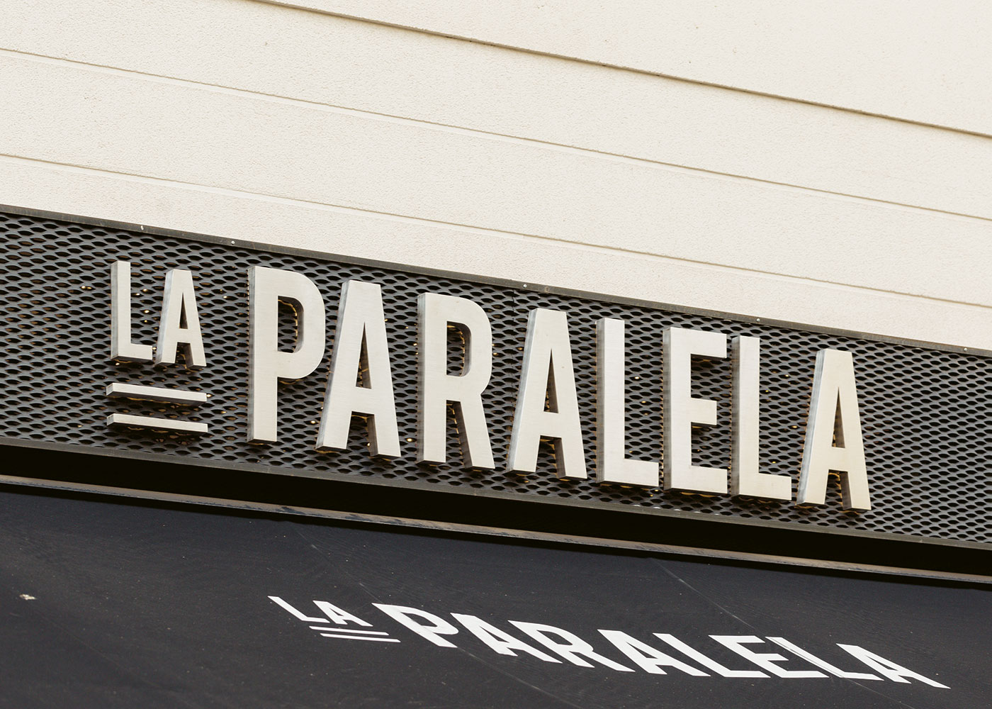 Imagen de los rótulos exteriores: letras en aluminio lacadas retroiluminadas mediante luz cálida y un toldo negro con el logotipo del restaurante "La Paralela"