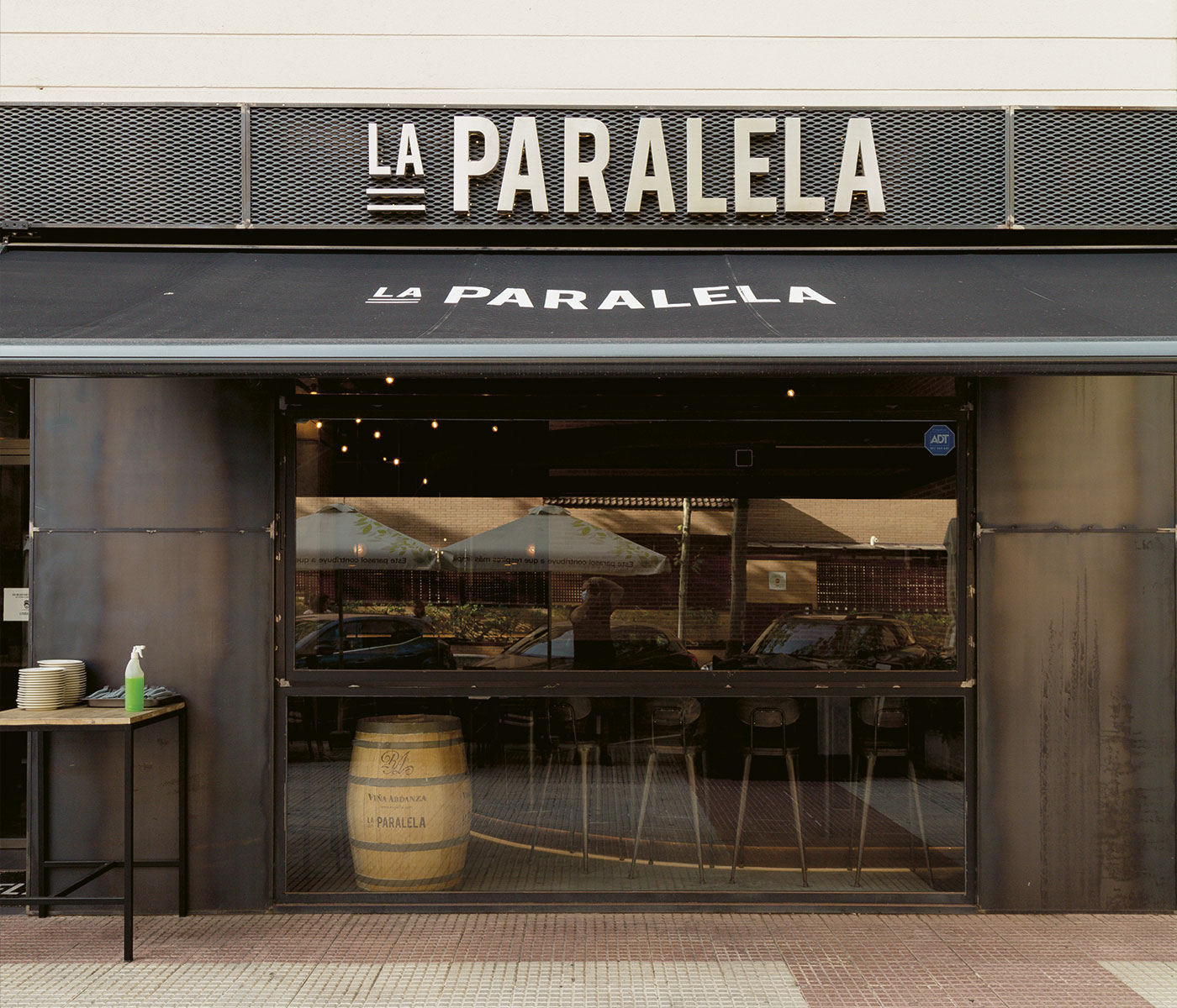 Imagen de los rótulos exteriores: letras en aluminio lacadas retroiluminadas mediante luz cálida y un toldo negro con el logotipo del restaurante "La Paralela"