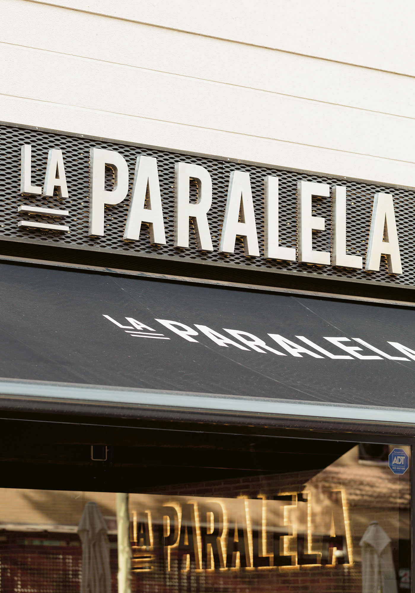 Imagen de los rótulos exteriores: letras en aluminio lacadas retroiluminadas mediante luz cálida y un toldo negro con el logotipo del restaurante "La Paralela"